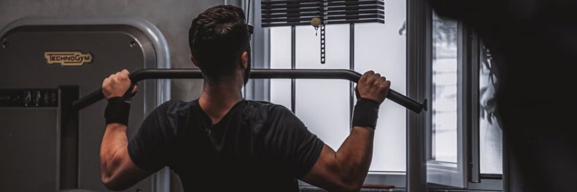 Back view of a man exercising with lat pulldown machine in the gym.